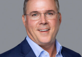 headshot of a middle-aged white man. He is smiling and wearing glasses.