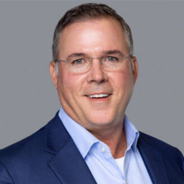 headshot of a middle-aged white man. He is smiling and wearing glasses.